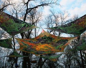 May include: A colorful, patterned canopy made of fabric hangs between trees in a forest. The canopy is made of a mesh-like material and has a variety of colors, including green, orange, and yellow.