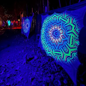 May include: A black fabric with a green and blue mandala design is illuminated with blacklight. The mandala is a geometric pattern with a starburst shape.
