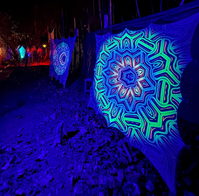 May include: A black fabric with a green and blue mandala design is illuminated with blacklight. The mandala is a geometric pattern with a starburst shape.