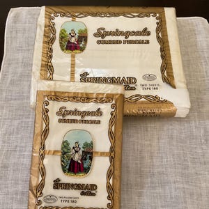 May include: Two packages of Springcale combed percale sheets and pillowcases. The packaging is white and gold with the Springmaid logo and a picture of a woman in a dress. The sheets are Type 180.