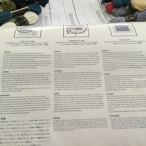 May include: A multi-lingual instruction sheet for a cross-stitch embroidery kit. The sheet includes instructions in English, French, German, Dutch, Spanish, Portuguese, Italian, Polish, and Japanese. The sheet also includes a diagram of the cross-stitch pattern.