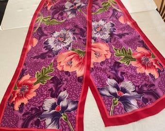 May include: A long, rectangular scarf with a vibrant floral pattern. The scarf features large flowers in shades of pink, purple, and peach, with green leaves against a magenta background. The edges are trimmed with a solid red border.