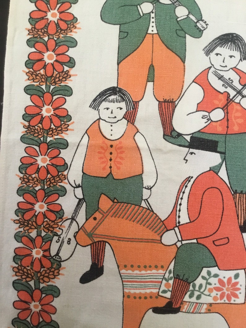 May include: A vintage fabric panel with a folk art design featuring four figures. Two figures are playing musical instruments, one figure is riding a rocking horse, and one figure is standing with a musical instrument. The background is a white fabric with a border of red flowers.