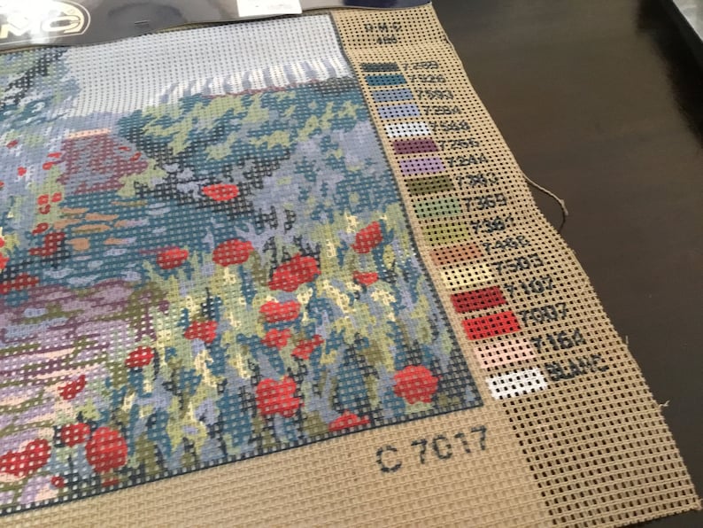 May include: A close-up of a cross-stitch pattern with a field of red poppies. The pattern is on a beige canvas with a color key and the number C 7017.