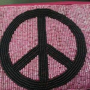 May include: A pink beaded clutch with a black peace sign design.