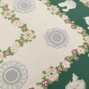 May include: A white tablecloth with a green and white floral pattern. The pattern features pink flowers, green leaves, and white teapots and cups.