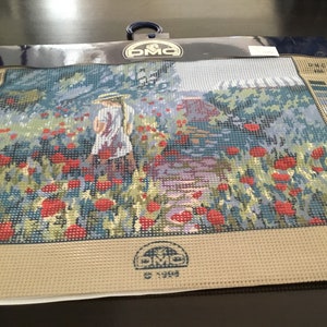 May include: A beige canvas with a printed design of a girl walking through a field of red poppies. The canvas is labeled "DMC" and "C 7017".