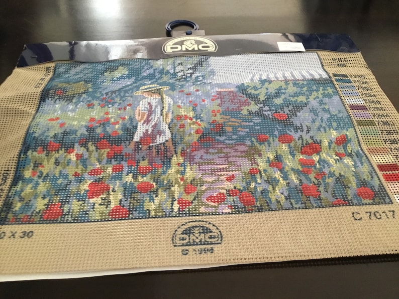 May include: A beige canvas with a printed design of a girl walking through a field of red poppies. The canvas is labeled "DMC" and "C 7017".