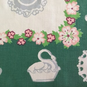 May include: A green fabric with a white and pink floral pattern. The fabric features a white swan, a white rabbit, and a white plate with a lace border.