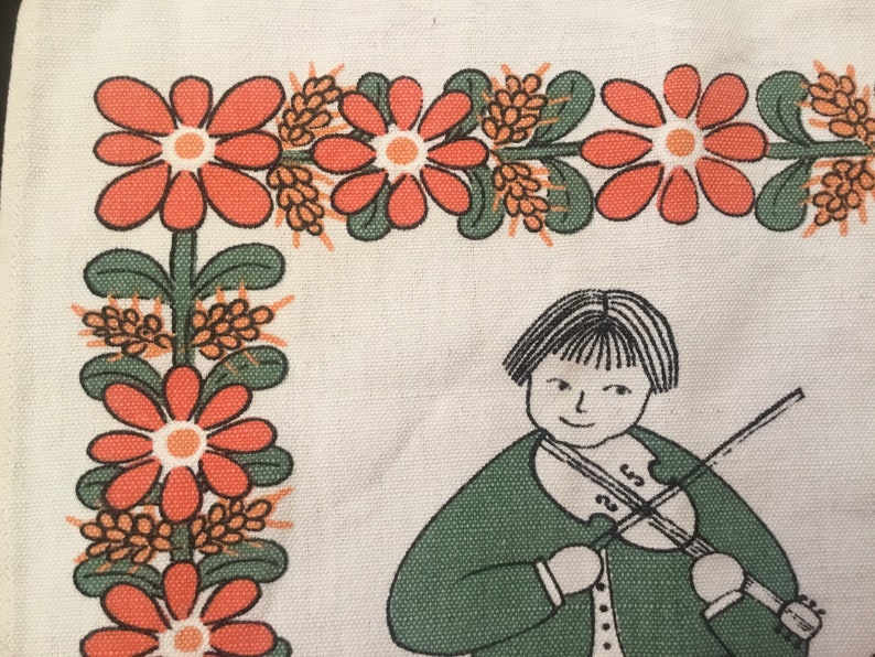 May include: A white fabric with a green, orange, and brown floral border. A girl with black hair is playing a violin in the center of the fabric.