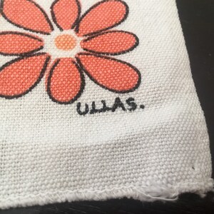 May include: White fabric with a red and orange flower design and the text "ULLAS." printed in black.