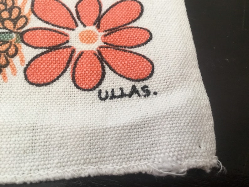 May include: White fabric with a red and orange flower design and the text "ULLAS." printed in black.