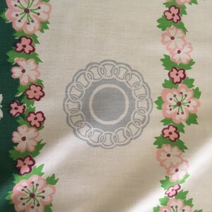 May include: A white tablecloth with a floral pattern in shades of pink, green, and grey. The tablecloth features a circular design in the centre with a grey background and a white border.
