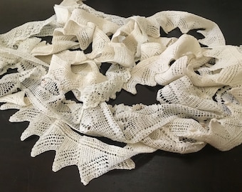 May include: A pile of white crocheted lace trim with a scalloped edge. The lace is delicate and intricate, with a variety of patterns.