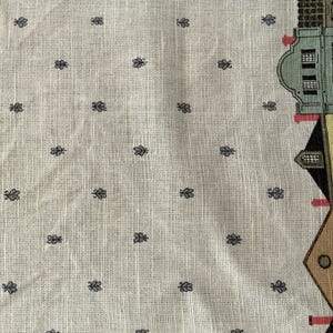 May include: Cream-colored fabric with a repeating pattern of small, dark blue floral motifs. The right edge features a partial illustration of buildings in various colors, including green, brown, and black. A decorative border runs along the bottom.
