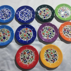 May include: Ten small ceramic plates with colorful floral designs. The plates are in shades of blue, green, purple, orange, and yellow. Each plate features a white background with a floral pattern in various colors.