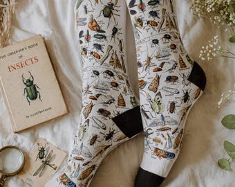 May include: White socks with a detailed insect illustration, featuring various bugs and a diagram-like layout. The socks have black heels and toes. A vintage book titled "The Observer's Book of Insects" and a magnifying glass are also visible.