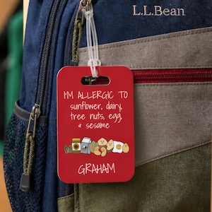 May include: A navy blue L.L.Bean backpack with a red tag that reads "I'M ALLERGIC TO sunflower, dairy, tree nuts, egg, & sesame" and the name "GRAHAM". The backpack is hanging in a wooden locker.