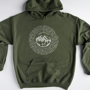 May include: A green hooded sweatshirt with a white graphic of a mountain range and the text "ADIRONDACKS 46" surrounded by a circle of text listing the names of the 46 Adirondack High Peaks.