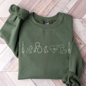May include: A dark green sweatshirt with a white outline of a syringe, cat, stethoscope, rabbit, heart with a heartbeat line, dog, and thermometer.