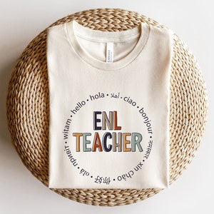 May include: A beige t-shirt with a circle graphic that says "ENL TEACHER" in colorful letters. The circle is surrounded by the word "hello" in English, Spanish, Arabic, Italian, French, Polish, and Russian.