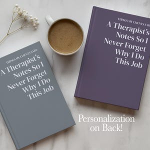 May include: Two hardcover journals, one gray and one purple, each featuring the white text: THINGS MY CLIENTS SAID: A Therapist's Notes So I Never Forget Why I Do This Job. A white ceramic mug filled with coffee and a small sprig of white flowers.