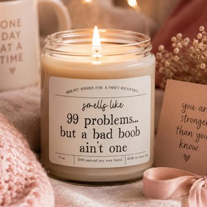 May include: A lit soy wax candle in a clear glass jar with a white label that reads: Breast wishes for a swift recovery. Smells like 99 problems... but a bad boob ain't one. 9 oz. 100% natural soy wax blend. 50-60 hrs burn time.