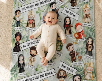 May include: A baby lies on a light green blanket with cartoon saints and the text "ALL YOU HOLY MEN AND WOMEN" and "PRAY FOR ME". The blanket has a tropical leaf design. The baby is on a beige surface.
