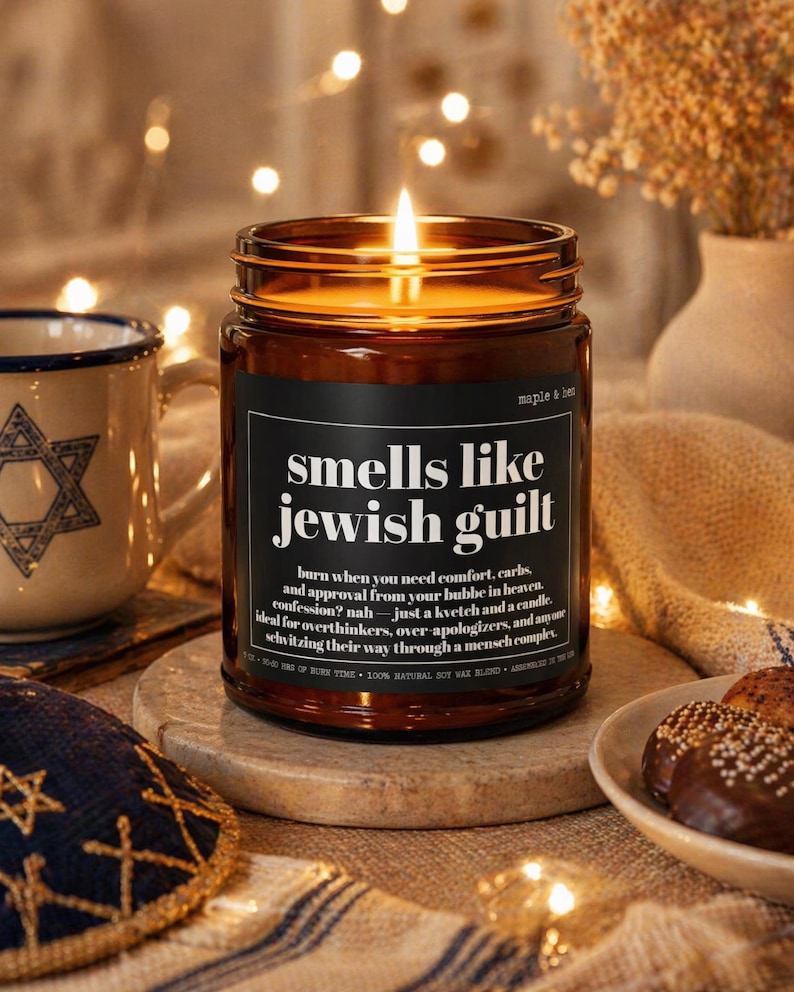May include: A lit candle in an amber glass jar with a black label featuring white text that reads: smells like jewish guilt, burn when you need comfort, carbs, and approval from your bubbe in heaven. Confession? nah&mdash;just a kvetch and a candle.