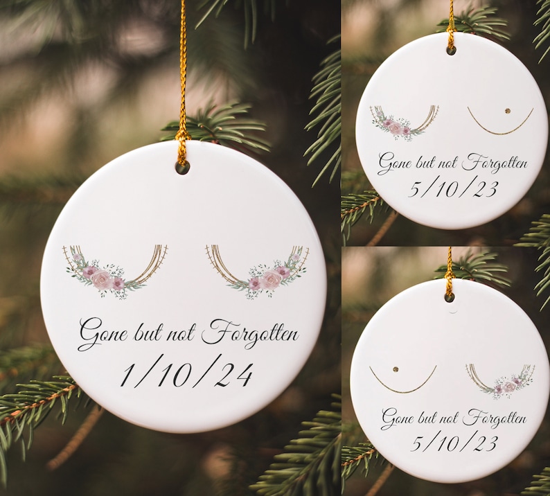 May include: Three white ceramic ornaments with gold string hangers. Each ornament features a stylized breast cancer awareness ribbon with pink flowers and the text "Gone but not Forgotten" with a date.