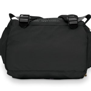 May include: Black messenger bag with two adjustable buckles and a shoulder strap. The bag has side pockets and a flap closure. The text "coven's newest little apprentice" is printed on the top of the bag.