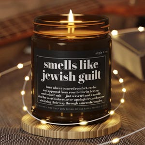 May include: A lit candle in a brown glass jar with a black label featuring the white text: smells like jewish guilt, burn when you need comfort, carbs, and approval from your bubbe in heaven. confession? nah &mdash; just a kvetch and a candle.