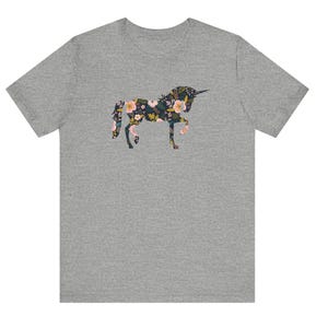 Puede incluir: Una camiseta gris con un dise&ntilde;o de unicornio floral. La silueta del unicornio est&aacute; llena de flores rosas, amarillas y azules sobre un fondo oscuro. La camiseta es una prenda casual.