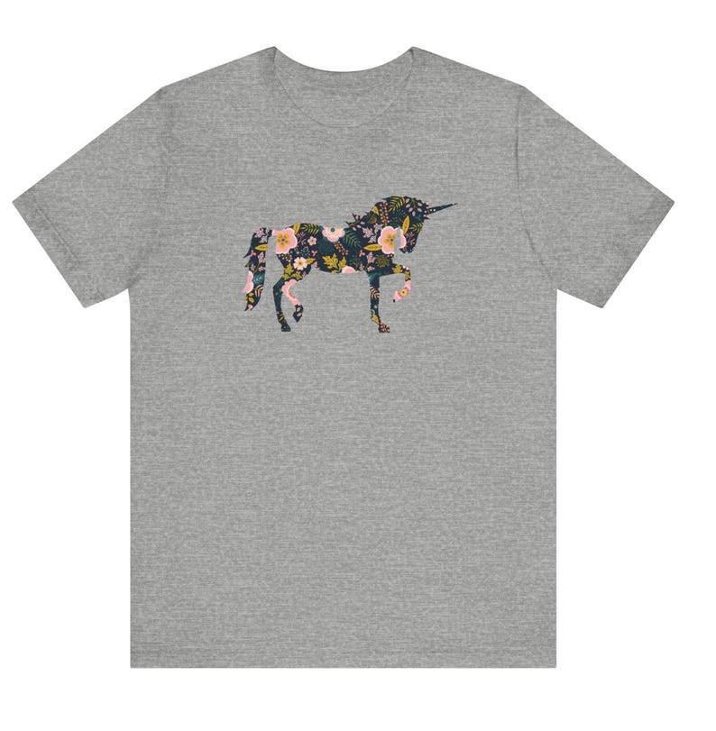 Puede incluir: Una camiseta gris con un dise&ntilde;o de unicornio floral. La silueta del unicornio est&aacute; llena de flores rosas, amarillas y azules sobre un fondo oscuro. La camiseta es una prenda casual.