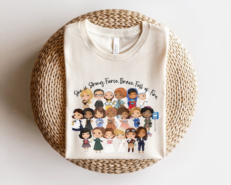 Pu&ograve; includere: T-shirt color crema con un gruppo di donne illustrate di diverse etnie e professioni. Il testo "She is Strong. Fierce. Brave. Full of Fire" &egrave; stampato sopra le illustrazioni. La maglietta &egrave; realizzata in un materiale morbido.