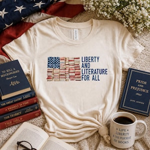 May include: Cream-colored t-shirt with the text "LIBERTY AND LITERATURE FOR ALL" and an American flag design made of books. The image includes books, a coffee mug, and an American flag.