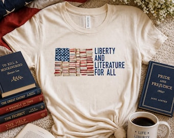 May include: A cream-colored t-shirt featuring the text "LIBERTY AND LITERATURE FOR ALL" and a flag design made of books. The image includes books, a coffee mug, and an American flag.