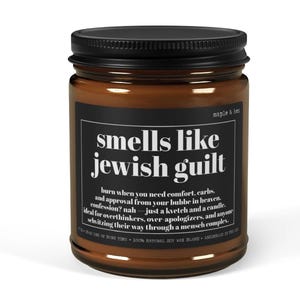 May include: A brown glass candle jar with a black lid and a black label featuring white text that reads: smells like jewish guilt, burn when you need comfort, carbs, and approval from your bubbe in heaven. confession? nah &mdash; just a kvetch and a candle.