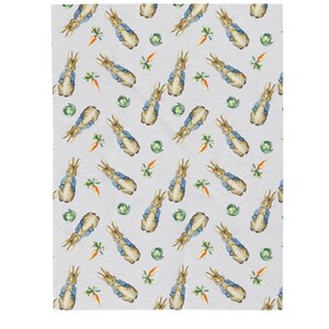May include: A light grey blanket with a repeating pattern of watercolour illustrations. The pattern includes rabbits in blue jackets, orange carrots, and green cabbages. The blanket is likely made of a soft, comfortable material.