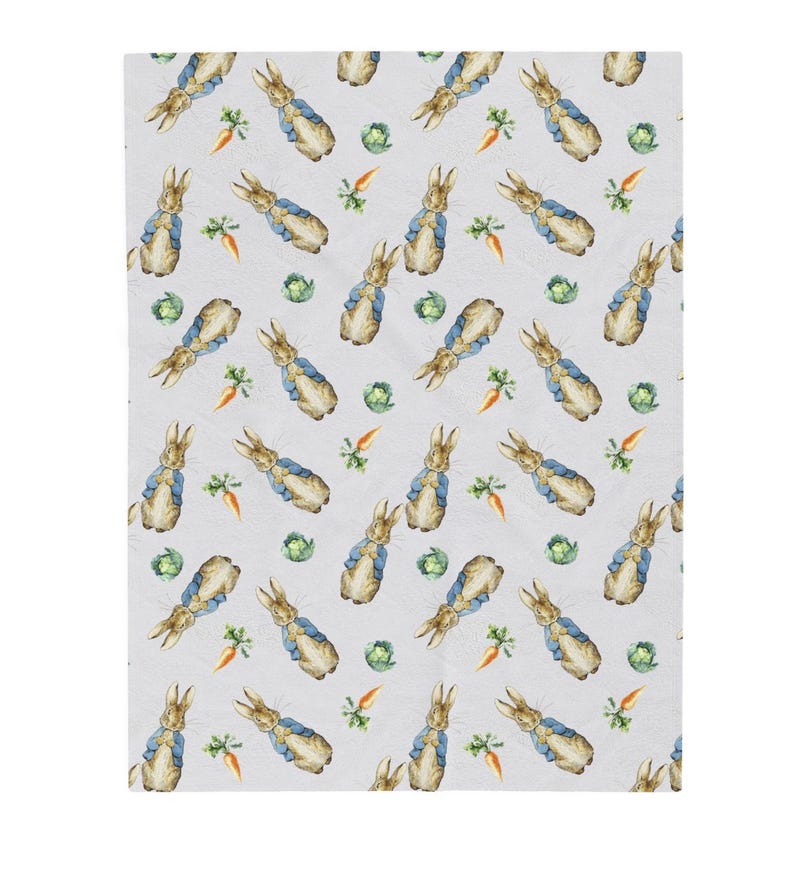 May include: A light grey blanket with a repeating pattern of watercolour illustrations. The pattern includes rabbits in blue jackets, orange carrots, and green cabbages. The blanket is likely made of a soft, comfortable material.