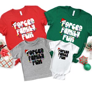 May include: A set of four t-shirts with a Christmas theme. The shirts feature the text "Forced Family Fun" with a Santa hat and Christmas lights. The shirts are in red, green, grey, and white.