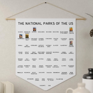 May include: A white fabric wall hanging with a wooden dowel and string for display. The text "THE NATIONAL PARKS OF THE US" is at the top, with a list of national parks below, each with a small image.