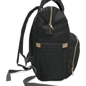May include: Black backpack with gold-colored zippers and a tan accent stripe. The backpack has a top handle, adjustable shoulder straps, and a side pocket with a zipper. The bag is made of a durable material and is designed for everyday use.
