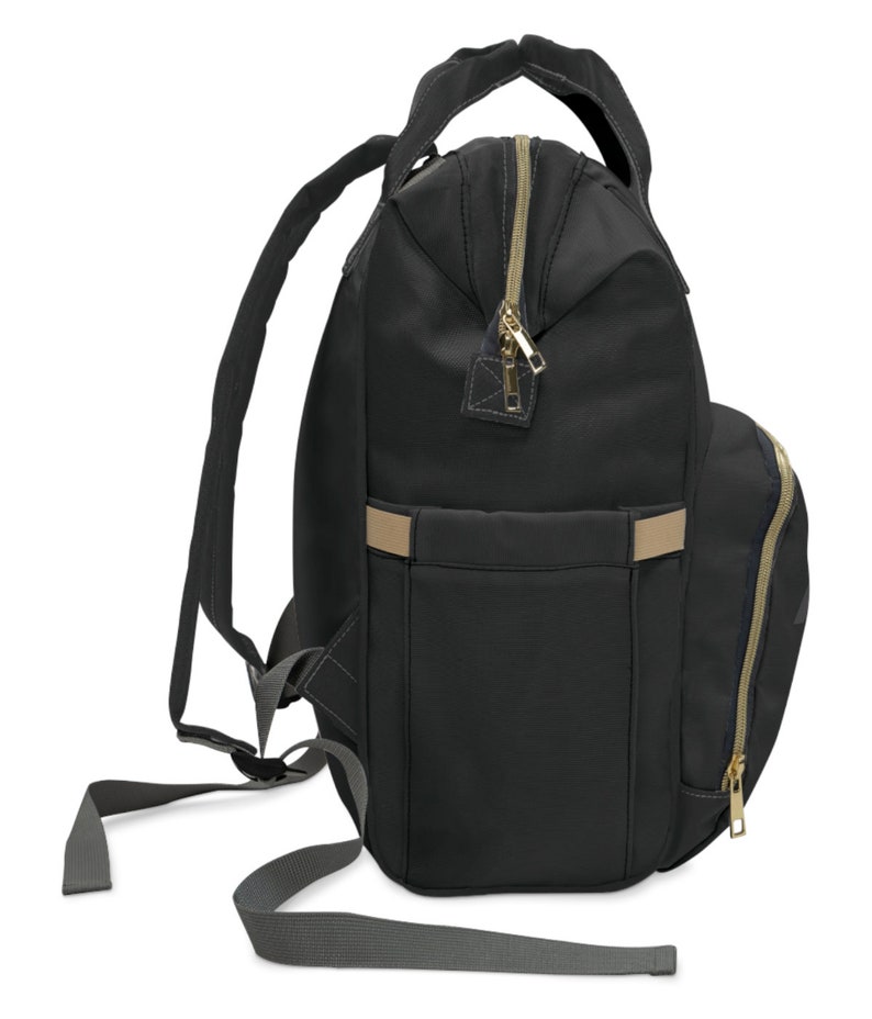 May include: Black backpack with gold-colored zippers and a tan accent stripe. The backpack has a top handle, adjustable shoulder straps, and a side pocket with a zipper. The bag is made of a durable material and is designed for everyday use.