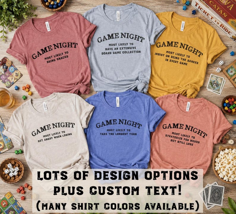 May include: Six short-sleeved t-shirts in mauve, light gray, mustard yellow, cream, blue, and coral. Each shirt features the black text GAME NIGHT followed by unique phrases like MOST LIKELY TO BRING SNACKS or MOST LIKELY TO TAKE THE LONGEST TURN.