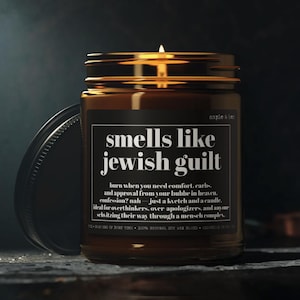 May include: A lit candle in an amber glass jar with a black label. The label features white text reading: smells like jewish guilt, burn when you need comfort, carbs, and approval from your bubbe in heaven. confession? nah&mdash;just a kvetch and a candle.