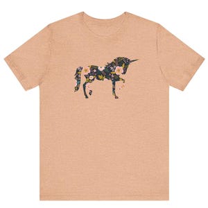 Puede incluir: Una camiseta color melocot&oacute;n con un dise&ntilde;o floral de unicornio. La silueta del unicornio est&aacute; llena de un patr&oacute;n de flores en tonos rosa, amarillo y verde. La camiseta tiene cuello redondo y mangas cortas, adecuada para uso casual.
