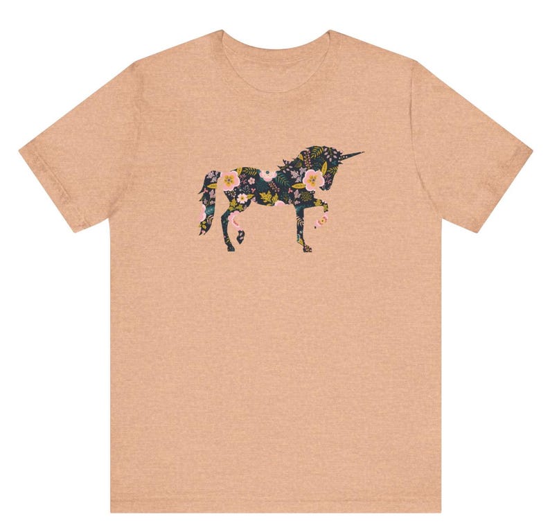 Puede incluir: Una camiseta color melocot&oacute;n con un dise&ntilde;o floral de unicornio. La silueta del unicornio est&aacute; llena de un patr&oacute;n de flores en tonos rosa, amarillo y verde. La camiseta tiene cuello redondo y mangas cortas, adecuada para uso casual.