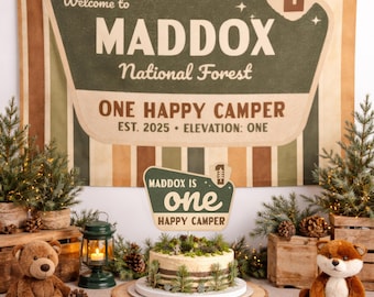 Könnte beinhalten: Eine Geburtstagsparty-Szene mit einem Hintergrund mit der Aufschrift "Welcome to Maddox National Forest". Ein Kuchen steht auf einem Holzständer, umgeben von Kiefern, einem Teddybär und einem Fuchs. Das Schild lautet "One Happy Camper".