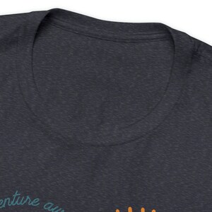 May include: Dark heather gray t-shirt with a V-neck collar. The shirt features the text "venture aw" in teal script. Below the text are orange dots. The shirt is made of a soft, comfortable material.